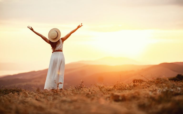 woman looking carefree in field with sunrise in the distance